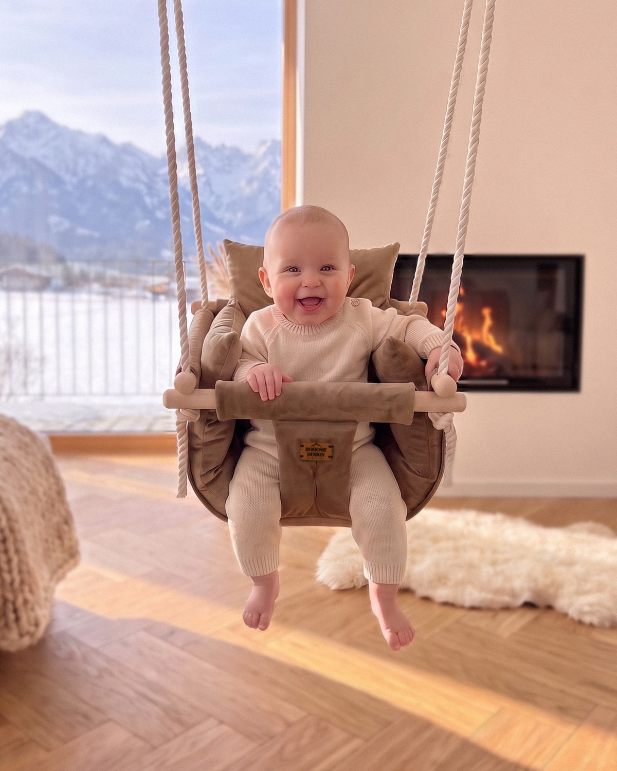 BOHOME Premium Babyschaukel Brown – fröhliches Baby in der handgefertigten Schaukel im Wohnzimmer mit Alpenblick